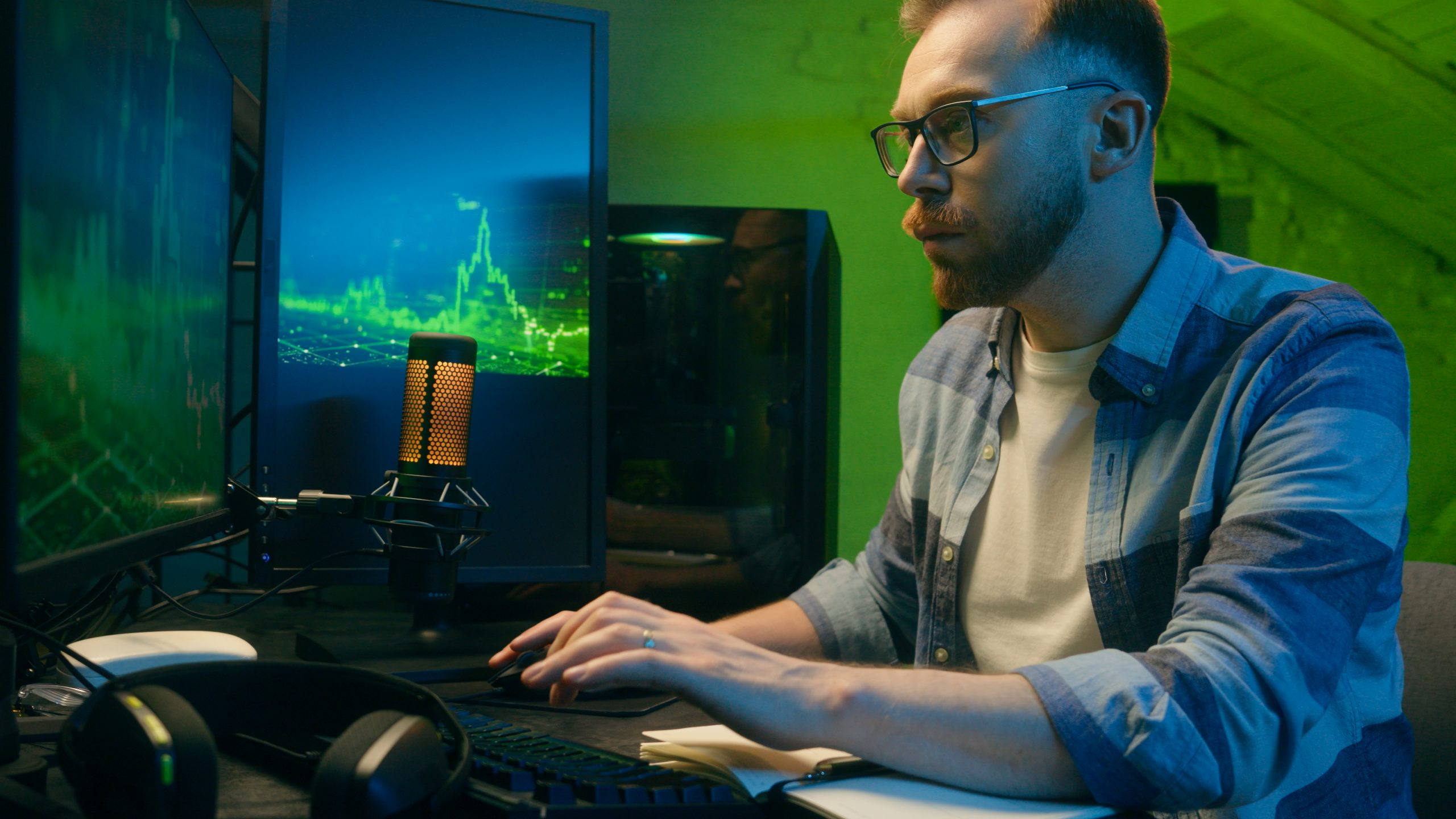 Profesiones clave en la industria de los videojuegos Hombre joven trabajando en una computadora con múltiples pantallas y micrófono profesional, en un entorno de estilo gaming.