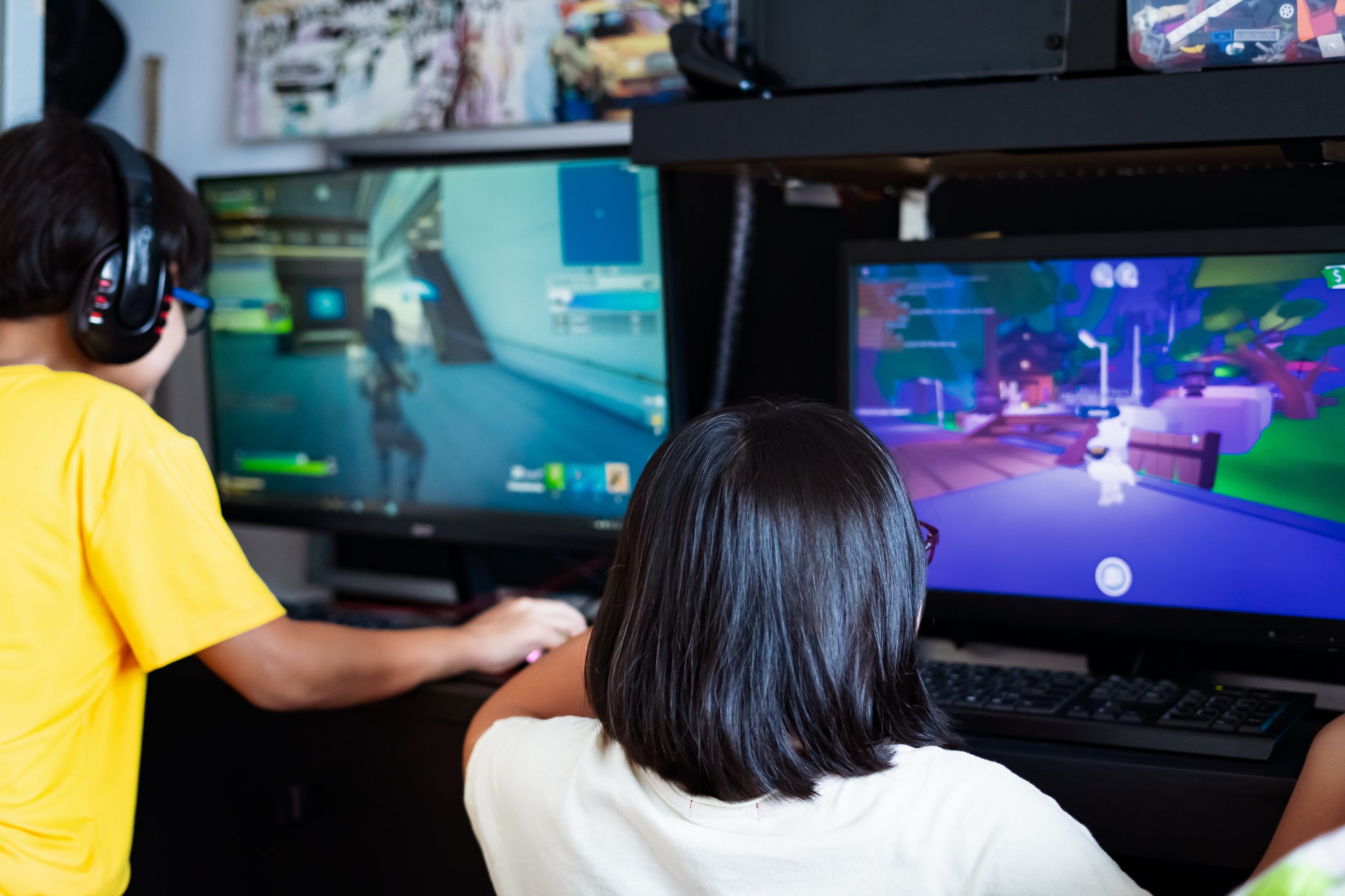 Dos niños juegan videojuegos en computadoras de escritorio, cada uno frente a su monitor.